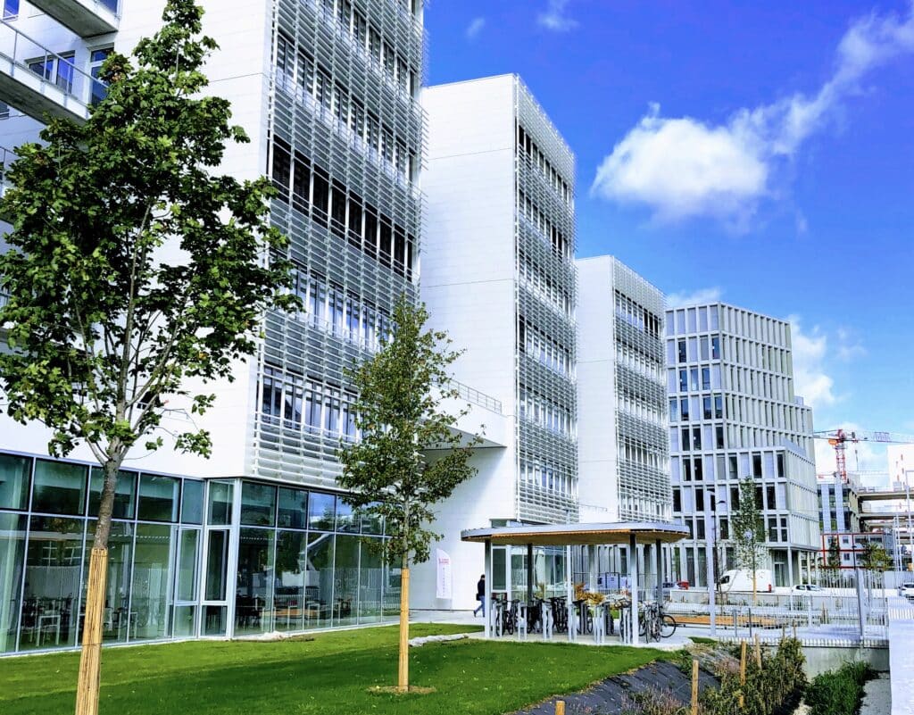 Photographie des bâtiments du Campus Condorcet : hautes tours blanches au design contemporain, espaces de stationnement pour vélos, jeunes arbres.