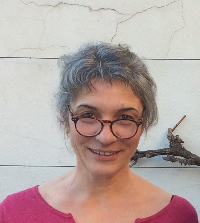 Photographie d'Agnès Gramain. Cheveux gris attachés, lunettes rondes et t-shirt rose, elle sourit à l'objectif.